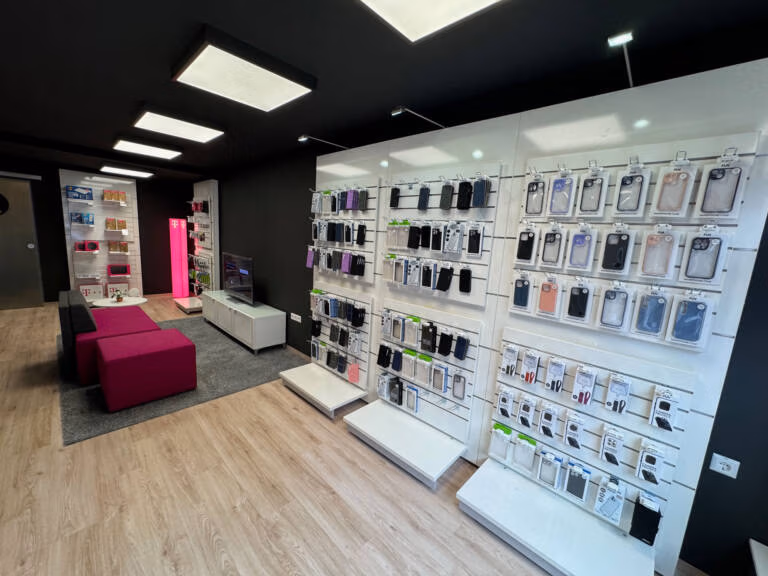 Tele-Planet ist ein modernes Geschäft für Telefonzubehör mit weißen Ausstellungswänden, an denen verschiedene Handyhüllen und Zubehör präsentiert werden. Rosa Stühle und ein grauer Teppich bereichern den Sitzbereich, während im Hintergrund Regale mit weiteren Produkten zu sehen sind.